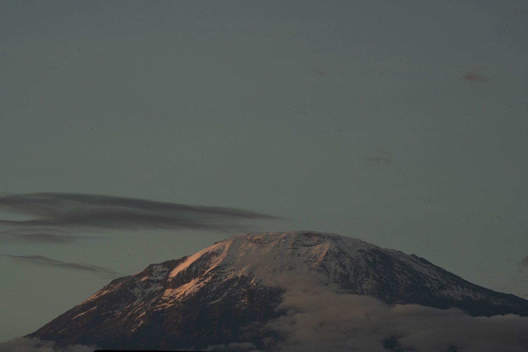 Snow-capped summit of Mount Kilimanjaro at dusk above the clouds