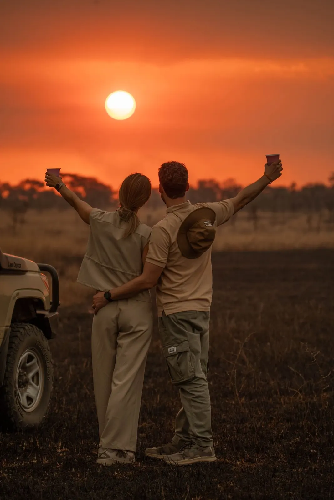 Pareja brindando al atardecer junto a su Land Cruiser de safari