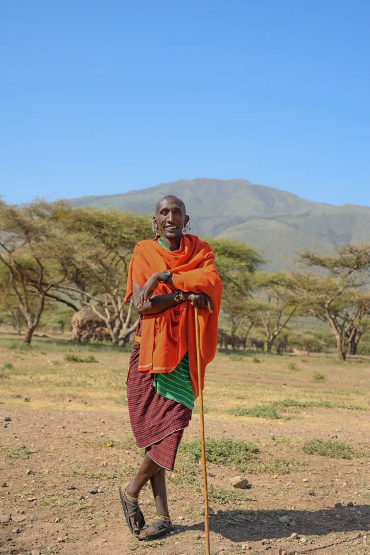 Maasai man smiling in front of acacia trees and the Ngorongoro highlands